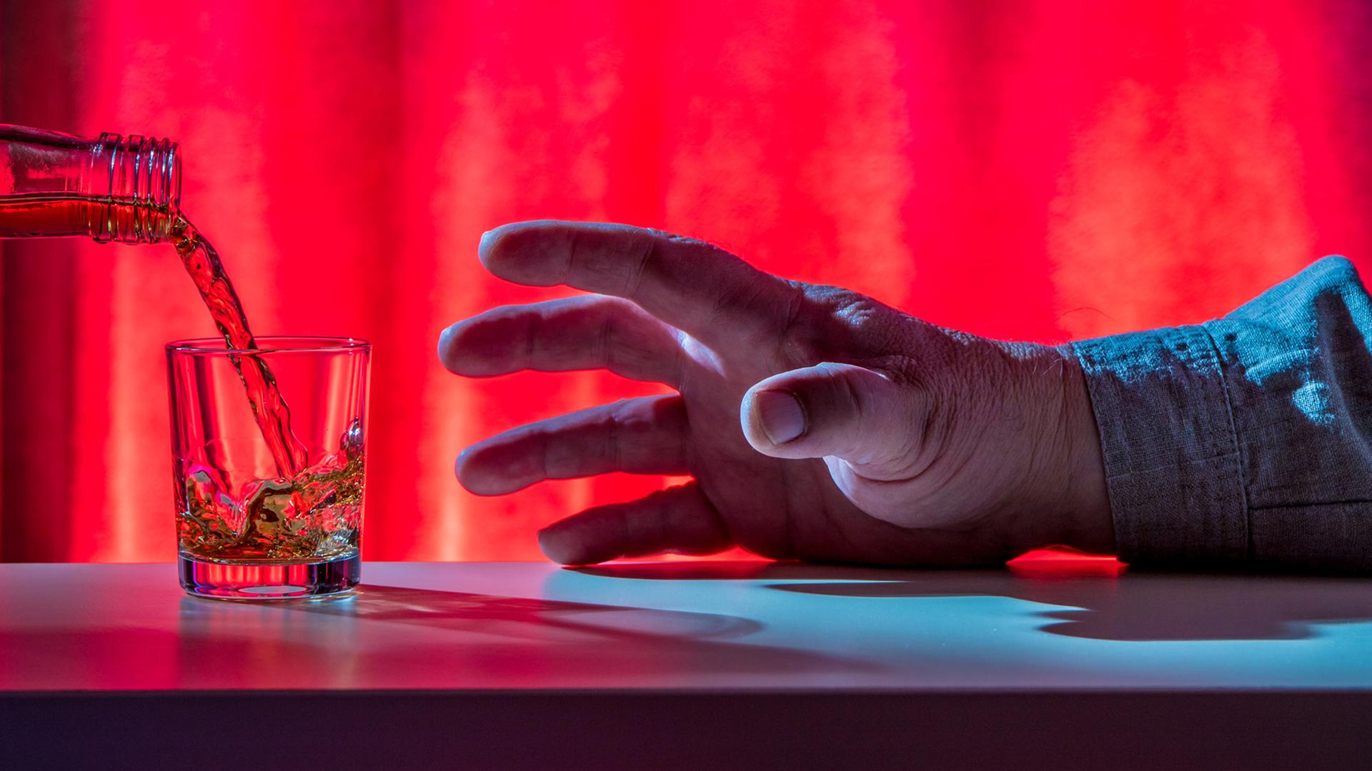 Eine Hand greift nach einem Schnapsglas.
