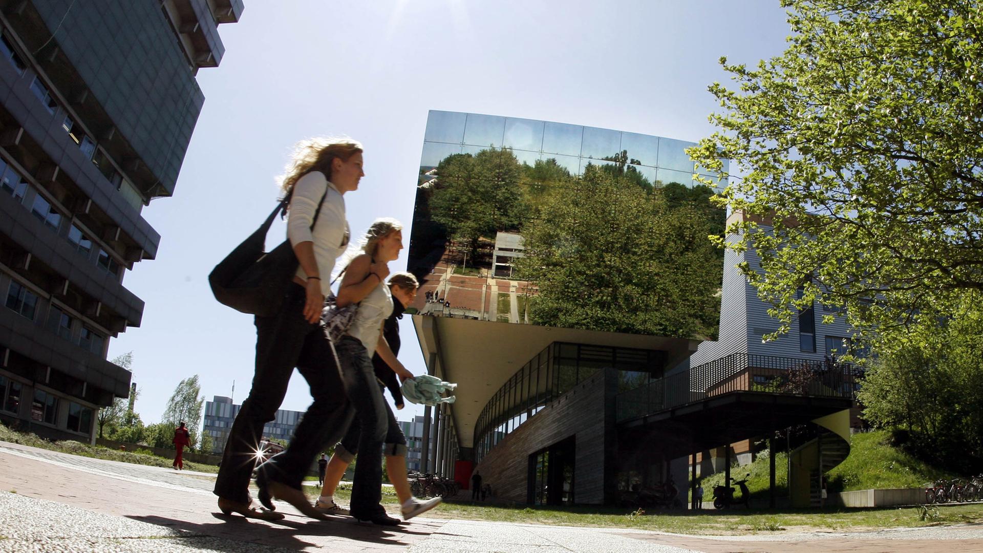Studentinnen der Justus-Liebig-Universität in Gießen gehen über den Campus für Naturwissenschaften mit seinem markanten, verspiegelten Gebäude im Zentrum.