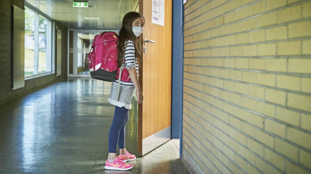 Ein Mädchen mit Mund-Nasen-Maske öffnet die Tür zu einem Klassenraum.