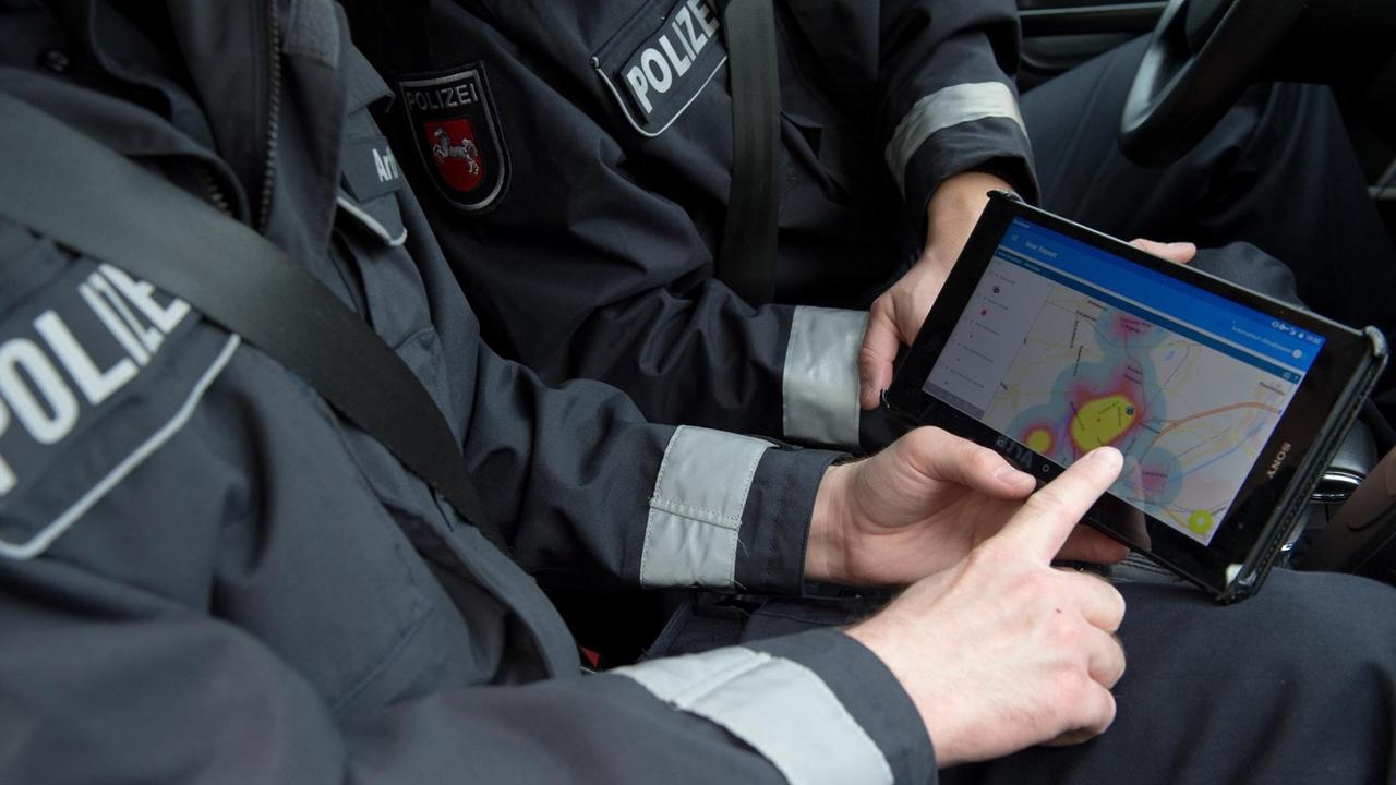 Ein Kommissar am Beifahrersitz zeigt auf ein Tablet-PC mit der Einbruchs-App "Premap" vom Landeskriminalamt, neben ihm sitz ein Kollege am Steuer.