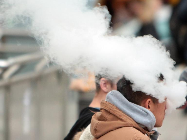 Ein junger Mann exhaliert den Rauch einer E-Zigarette in Frankfurt am Main in Hessen