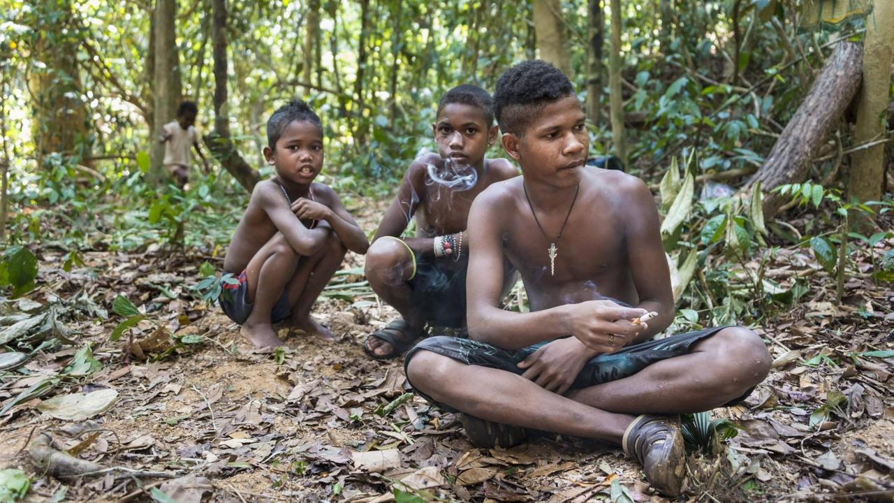 Drei Jungen der Orang Asli sitzen auf dem Boden im Dschungel und rauchen