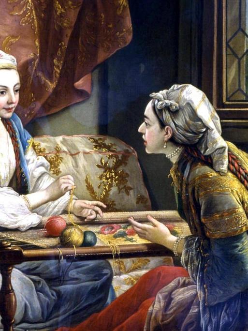 Eine junge Frau in orientalischem Gewand sitzt stickend einer andenen Frau auf großen Kissen gegenüber.