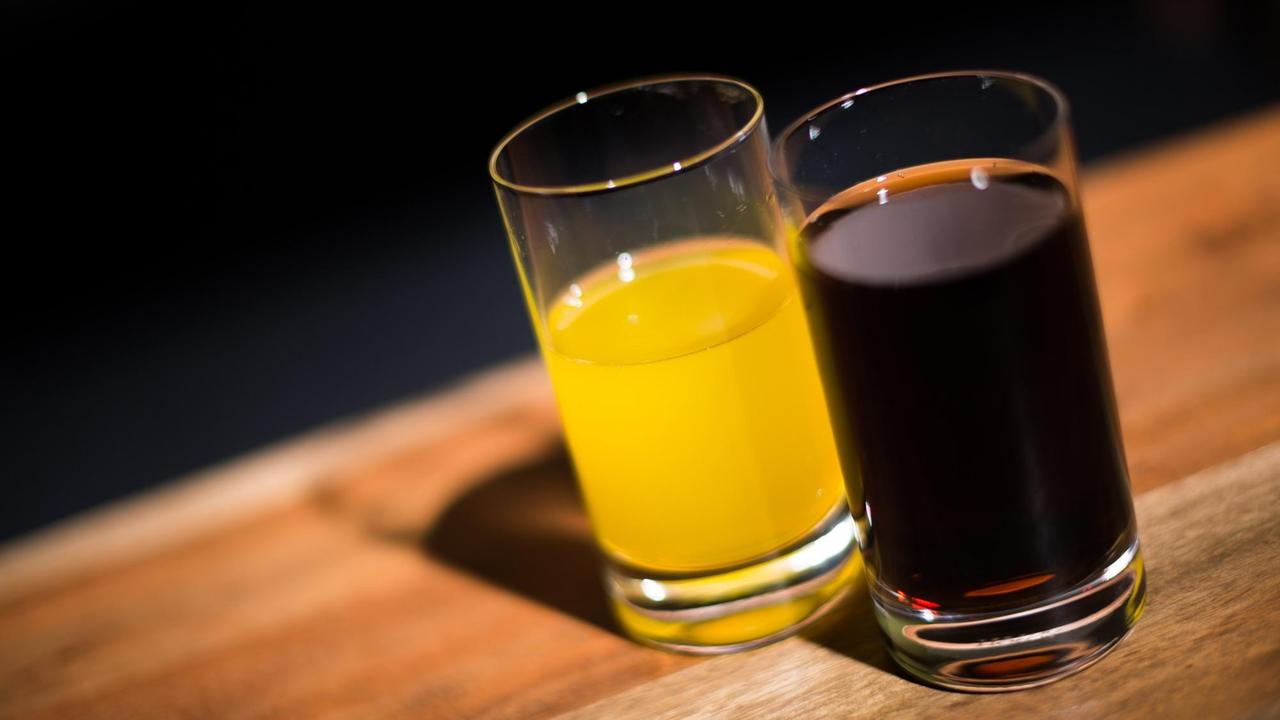 Ein Glas mit Cola steht neben einem Glas mit Orangenlimonade.