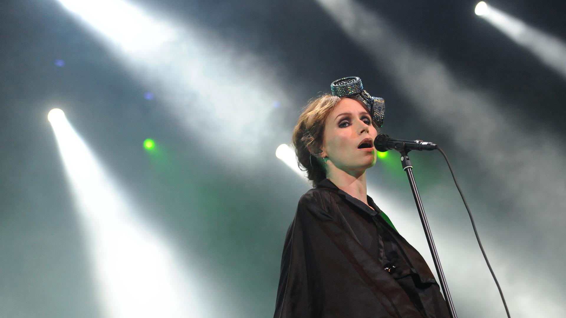 Die Sängerin Nina Persson steht auf einer Bühne im hellen Licht einzelner Scheinwerfer