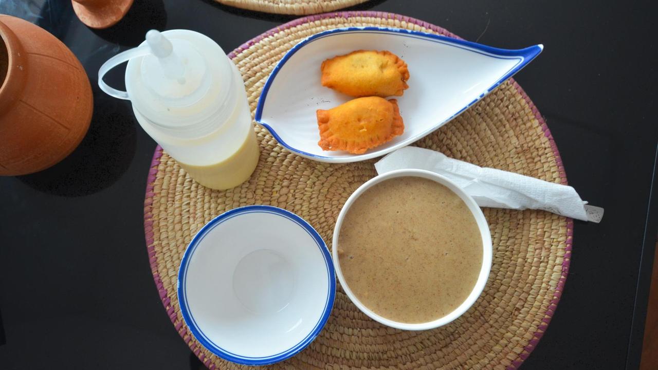 Auf einem Tisch steht ein Teller mit Bouillies, einem traditionellen Brei aus geschrotetem oder gemahlenem Getreide, sowie ein Schale mit zwei ausgebackenen Teigtaschen.