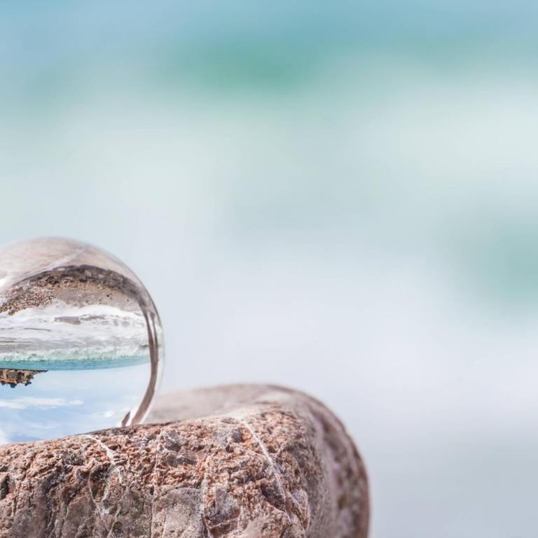 In einer Glaskugel spiegelt sich die Adriaküste, die im Hintergrund nur unscharf zu sehen ist.