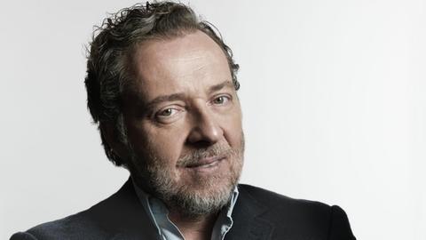 Der Bariton Christian Gerhaher blickt in die Kamera, hält die Arme verschränkt.