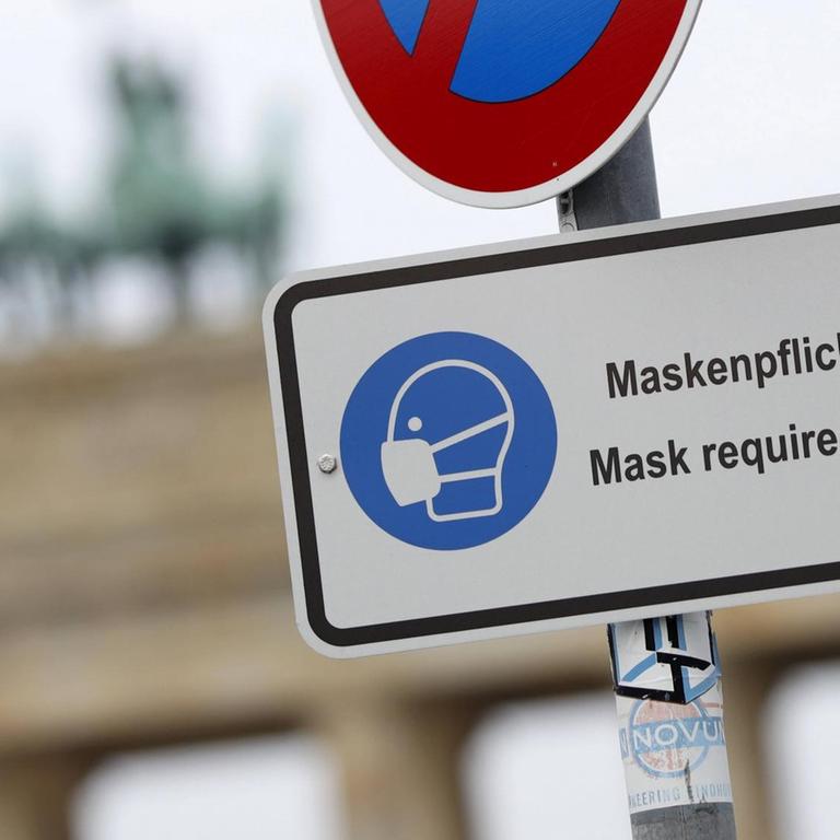 Vor dem Brandenburger Tor in Berlin weist ein Schild auf die Maskenpflicht hin