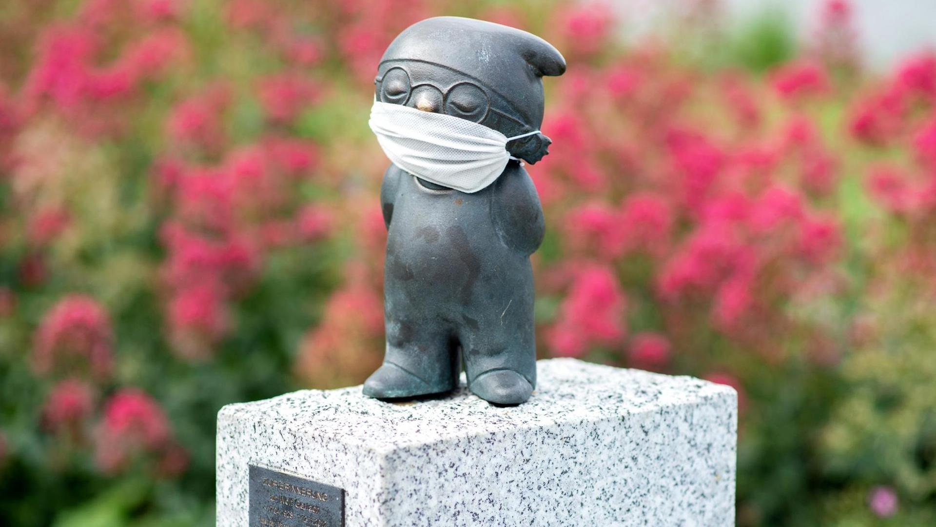 Eine Bronzefigur von einem ZDF-Mainzelmännchen, bekleidet mit einem Mund-Nasen-Schutz