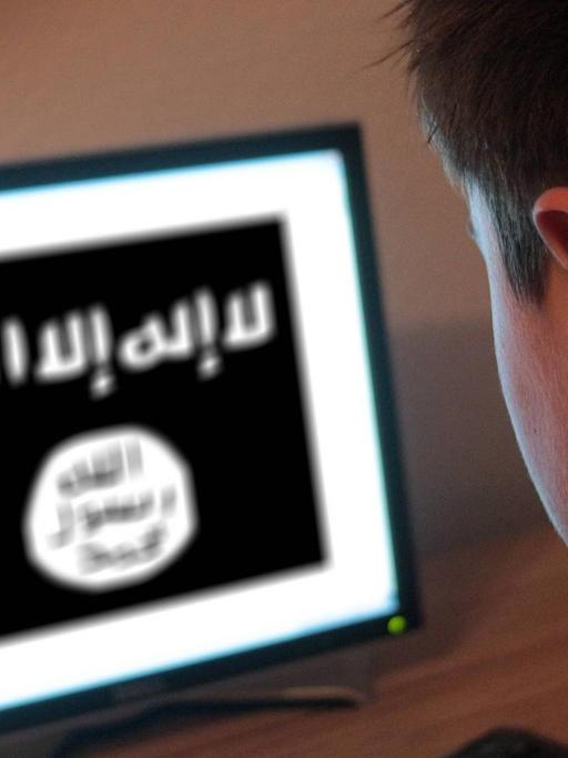 Ein Jugendlicher sitzt am Bildschirm eines PCs, der die Flagge der Terrormiliz IS zeigt.