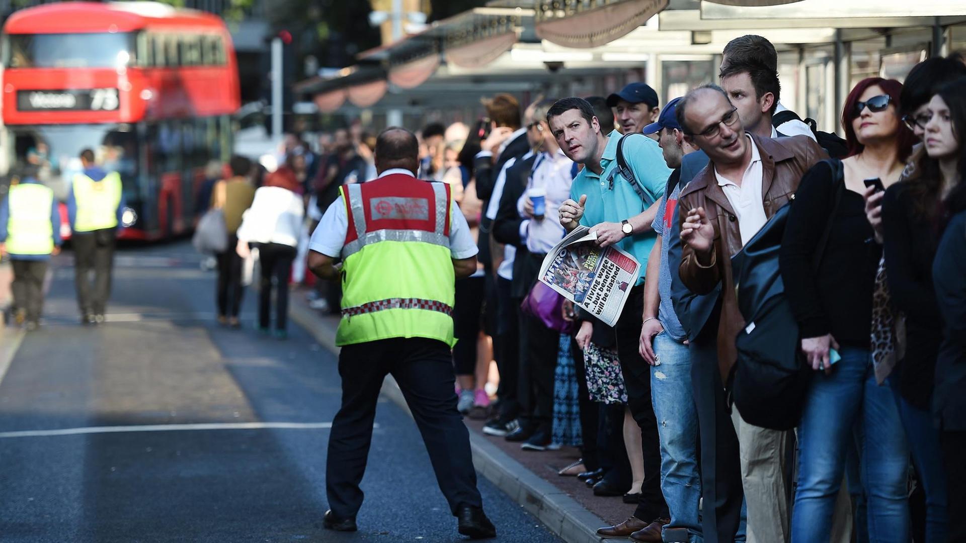 Viele Menschen drängen sich an einer Haltestelle in London, im Hintergrund fährt ein roter Doppeldecker-Bus. Viele Menschen drängen sich an einer Haltestelle in London, im Hintergrund fährt ein roter Doppeldecker-Bus.