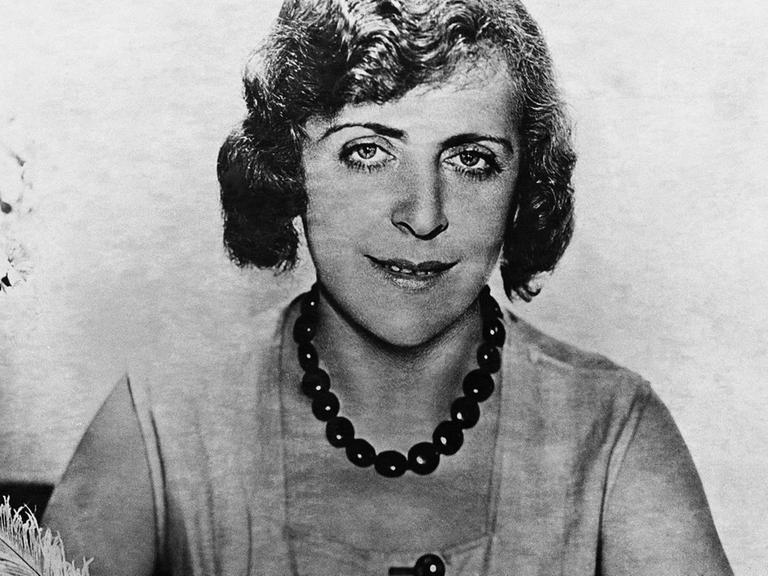 Vicky Baum 1931 in Hollywood, schreibt an einem Tisch mit einer Feder und guckt in Richtung Kamera.