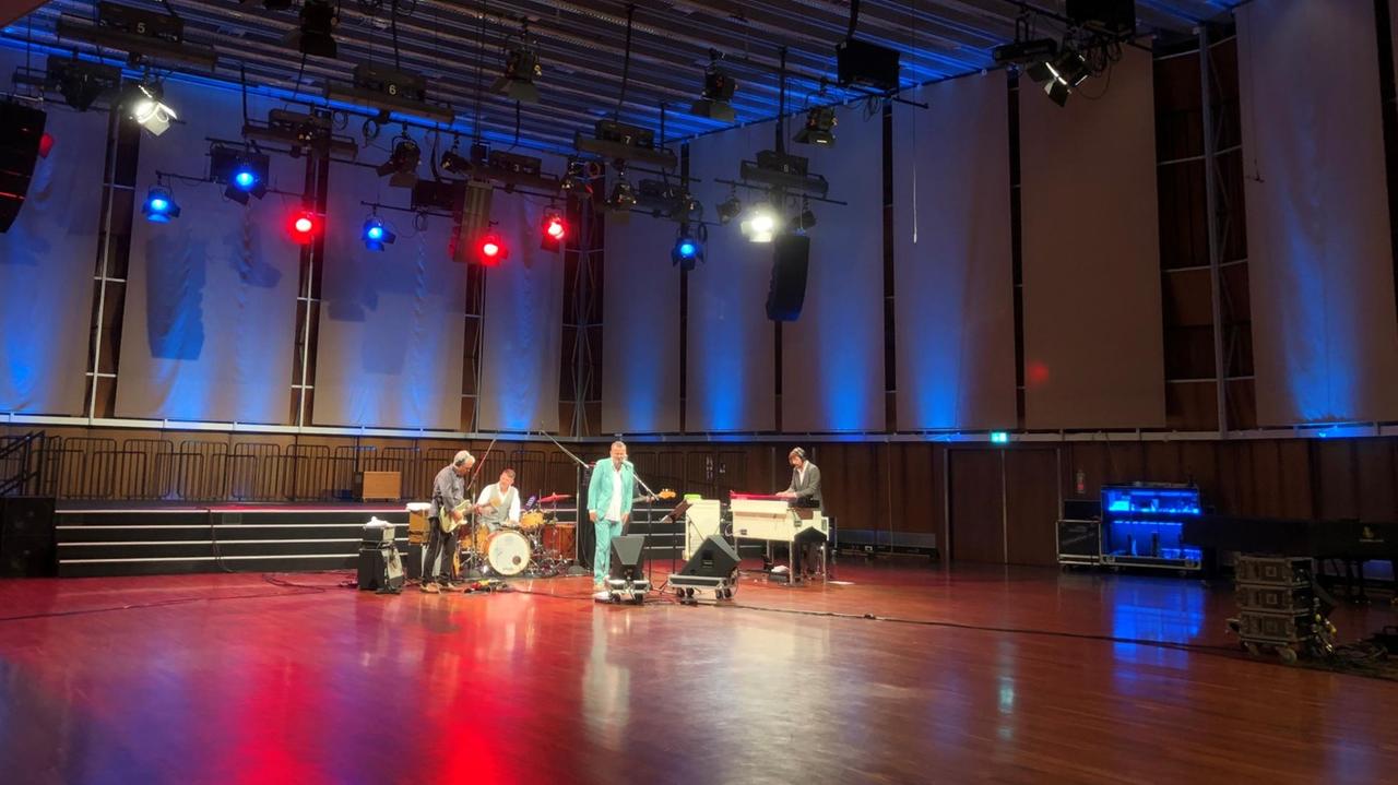 Fünf Musiker stehen mit ihren Instrumenten im 500 Quadratmeter großen Saal, der von bunten Scheinwerfern erleuchtet wird.