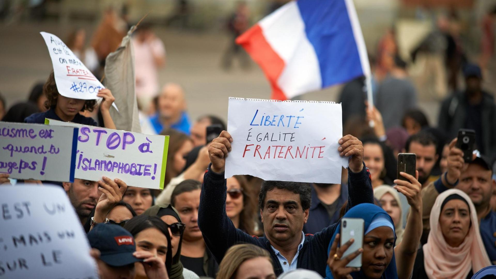 Menschen versammelten sich gegen Islamophobie auf dem Hauptplatz von Toulouse, der Capitole. Ein Mann zeigt eine Zeitung mit dem französischen Motto "Freiheit, Gleichheit, Brüderlichkeit".