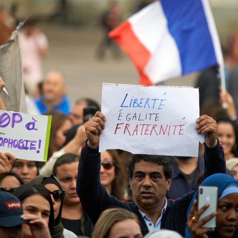 Menschen versammelten sich gegen Islamophobie auf dem Hauptplatz von Toulouse, der Capitole. Ein Mann zeigt eine Zeitung mit dem französischen Motto "Freiheit, Gleichheit, Brüderlichkeit".  
