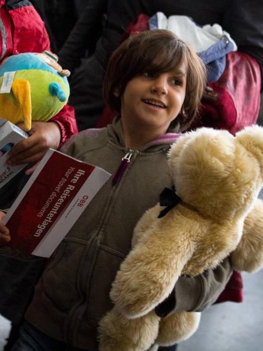Flüchtlingskind mit einem Teddybär im Arm auf dem Bahnhof.