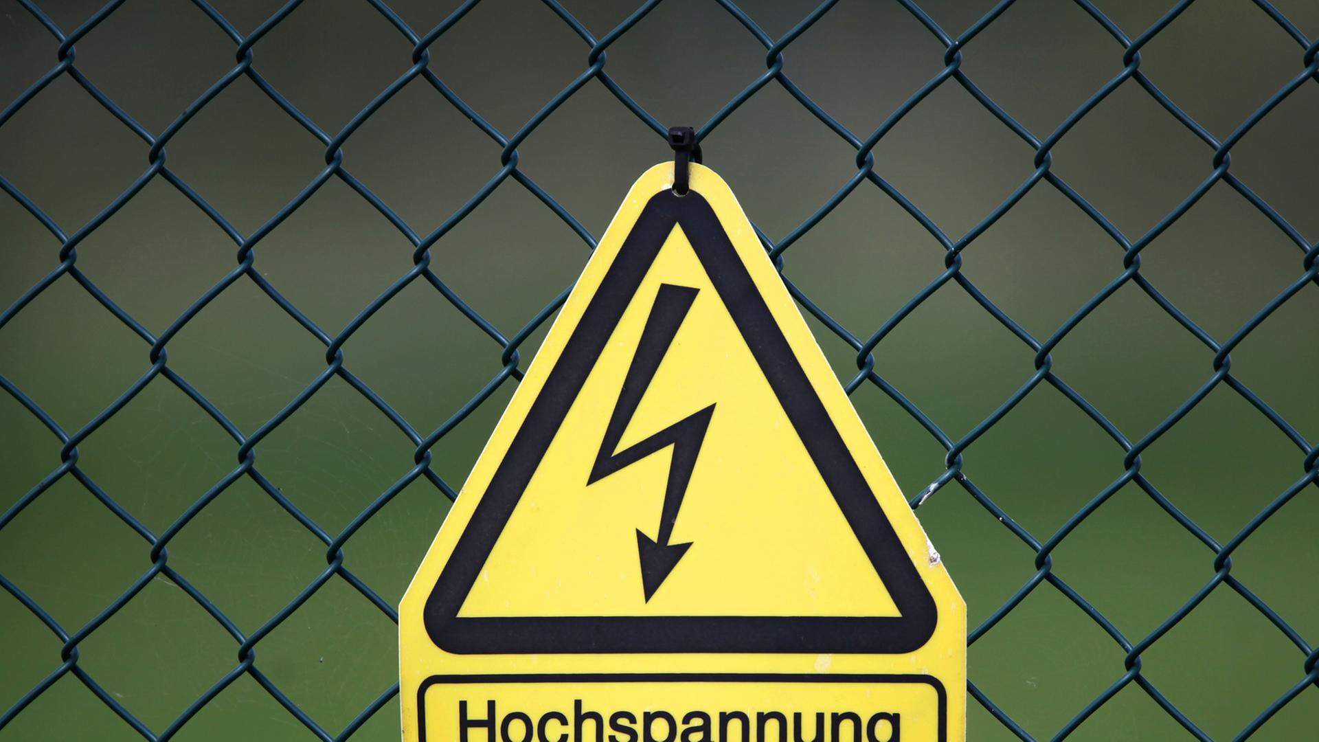Ein Schild warnt an einem Maschendrahtzaun vor Lebensgefahr durch Hochspannung.