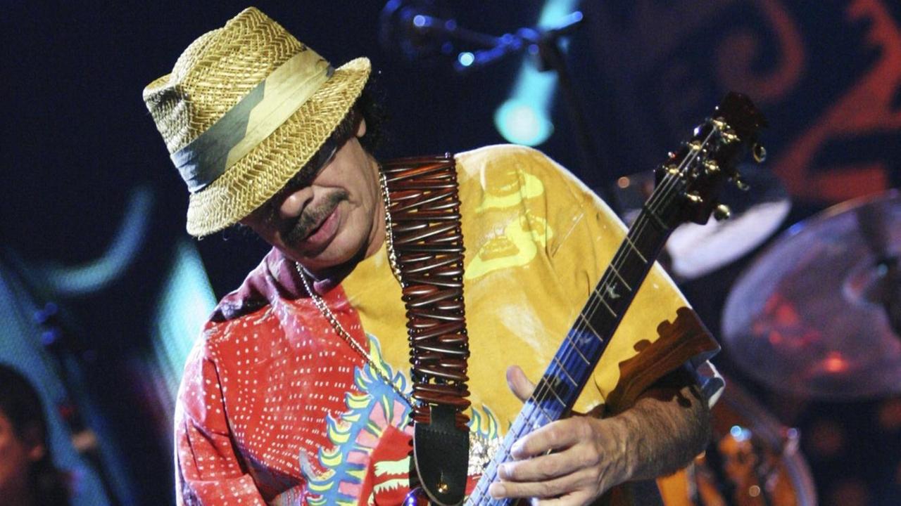 Der Musiker Carlos Santana beim Gitarrespiel mit buntem Hemd und Strohhut.