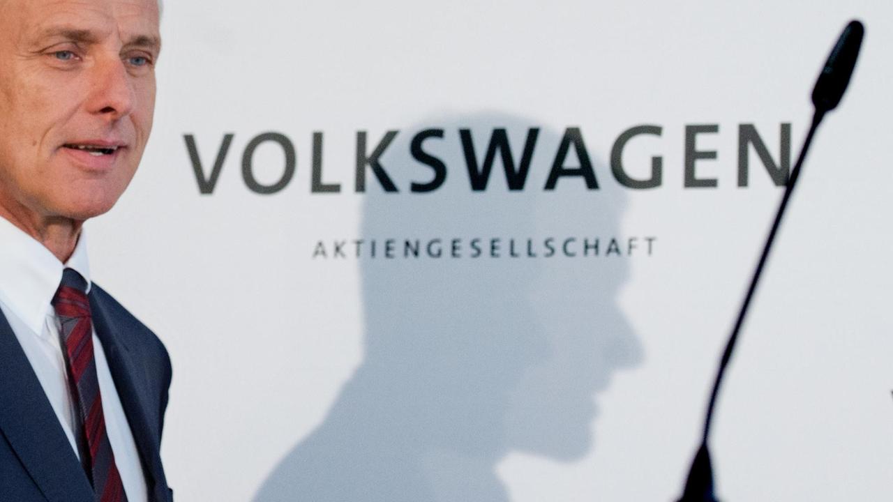 Müller auf dem Weg zu einem Mikrofon bei einer Pressekonferenz. An der weißem Wand hinter ihm steht "Volkswagen Aktiengesellschaft".