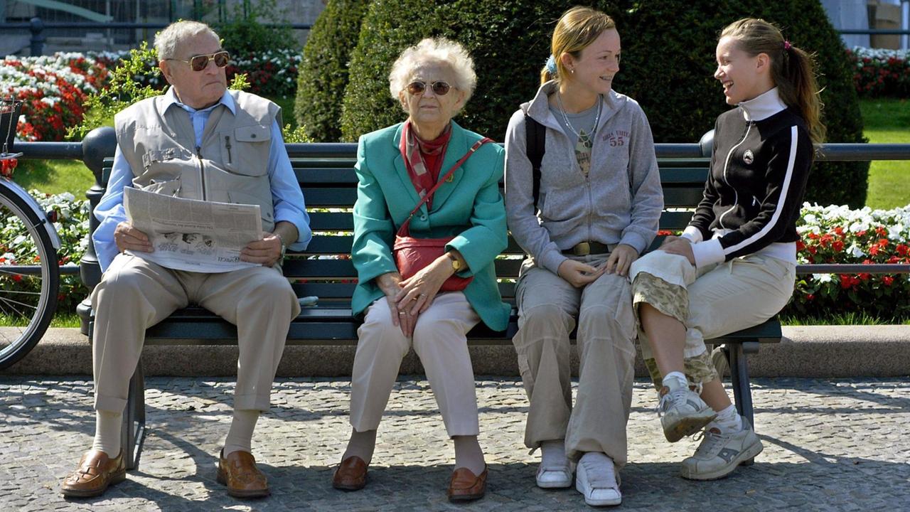 Ein Rentnerpärchen sitzt am 22.08.2003 auf einer Bank neben zwei jungen Mädchen auf dem Pariser Platz am Brandenburger Tor in Berlin