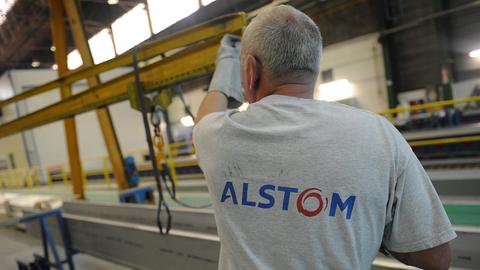 Ein Mann in einer Industriehalle ist von hinten zu sehen. Auf seinem T-Shirt steht der Aufdruck "Alstom".