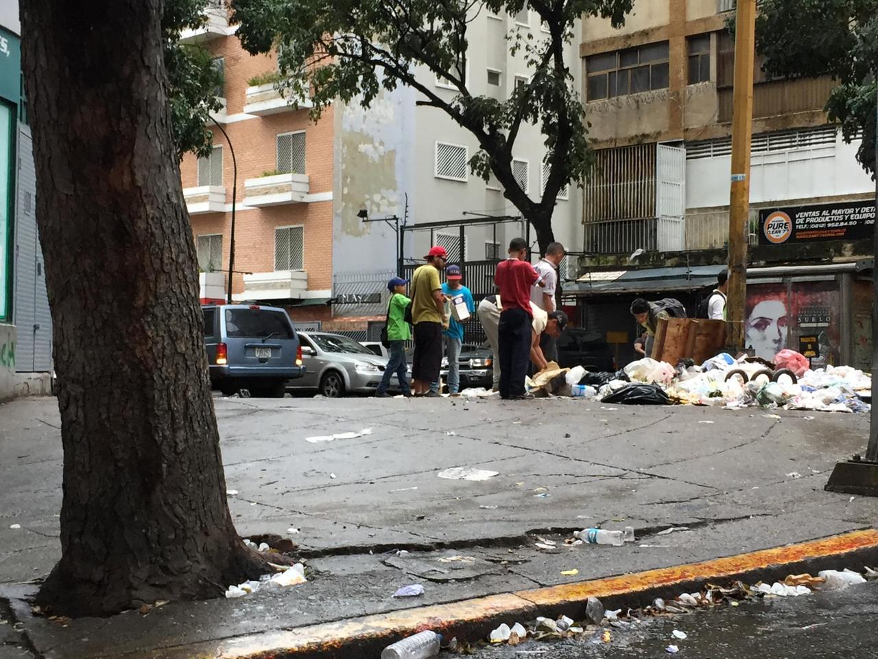 Auf einer Straße in Caracas wühlen junge Männer in Mülltüten.