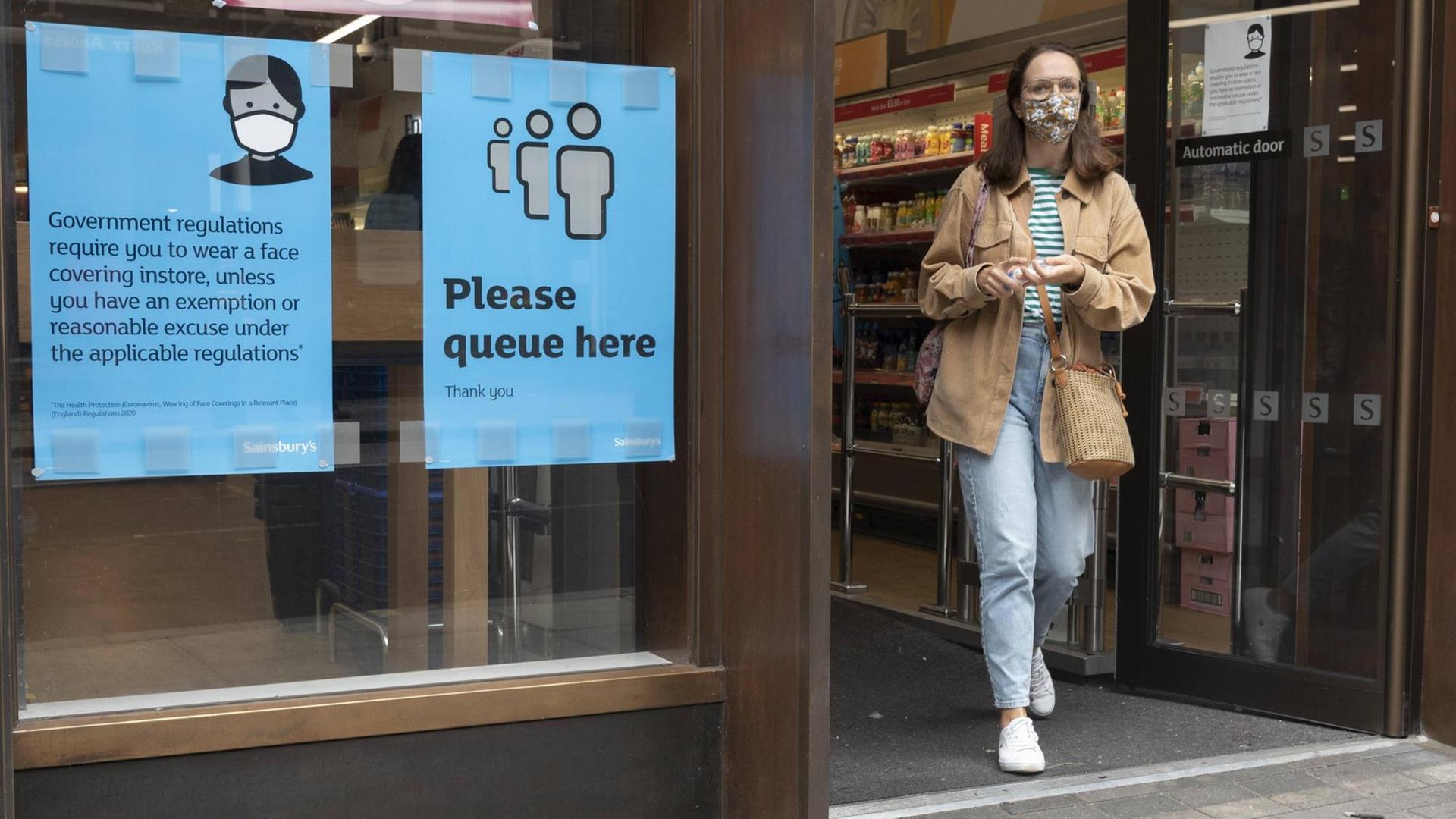 Eine Frau mit Corona-Schutzmaske verlässt einen Supermarkt in London.