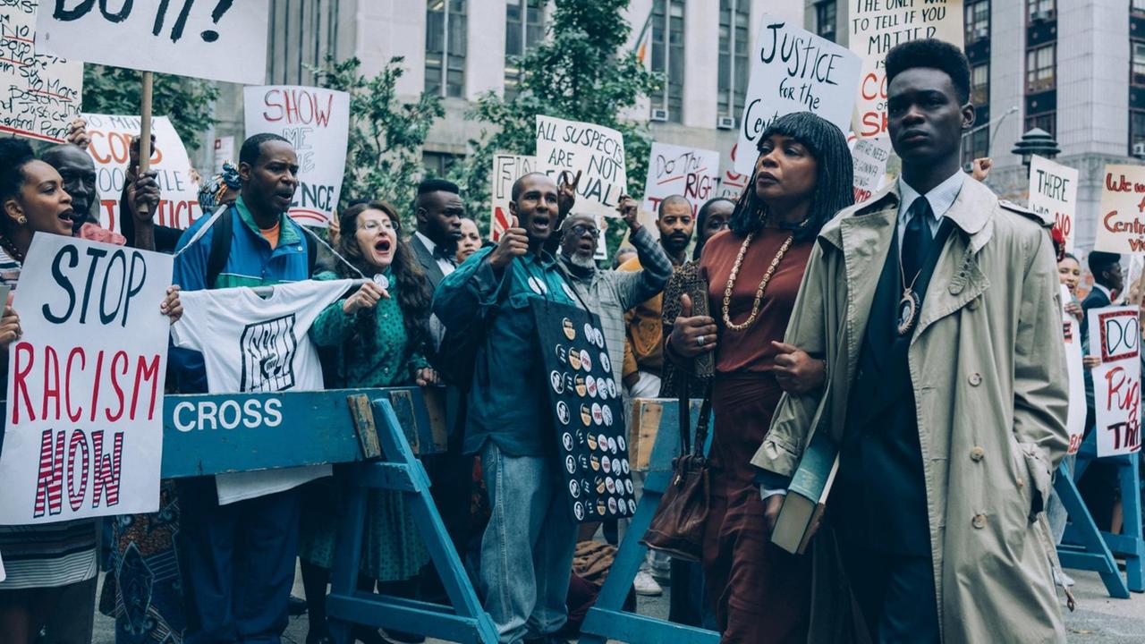 Eine schwarze Frau und ein schwarzer Mann gehen an einer Demo von Anti-Rassismus-Aktivisten vorbei.
