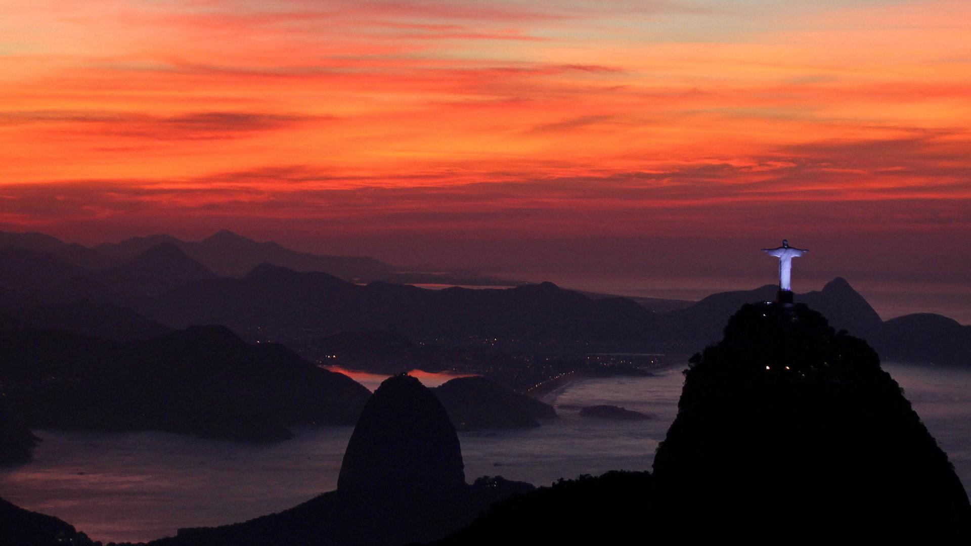 Die berühmte Christusstatue in der Bucht von von Rio de Janeiro erscheint in der Abenddämmerung vor einem rot leuchtenden Himmel.
