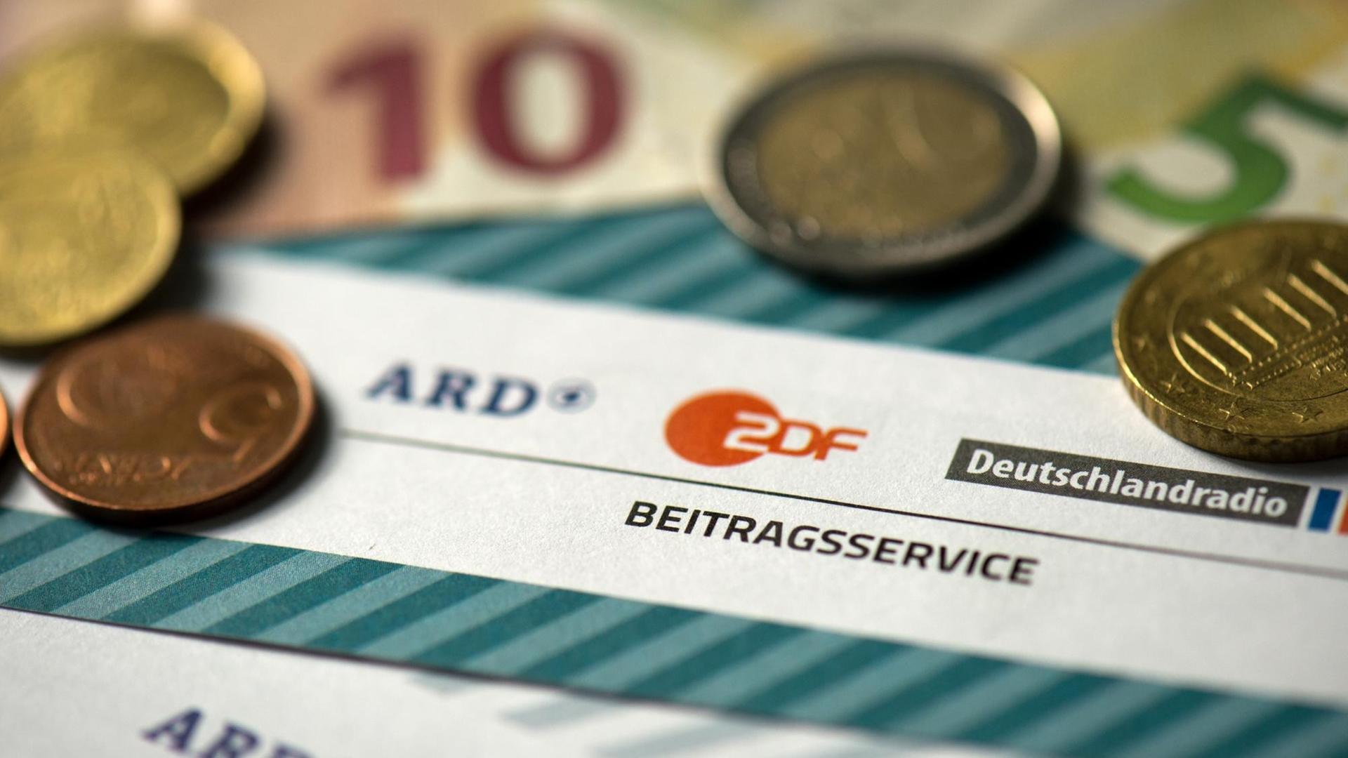 Münzgeld liegt auf Formularen für den Rundfunkbeitrag von ARD, ZDF und Deutschlandradio