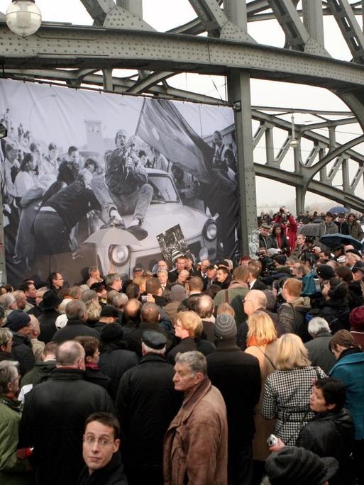 Das Bild zeigt wie an der Brücke an der Bornholmer Straße große Menschenmassen versuchen, einen Blick auf Bundeskanzlerin Angela Merkel, den ehemaligen Sowjetpräsidenten Michail Gorbatschow und den ehemaligen polnischen Solidaritätsführer Lech Walesa zum 20. Jahrestag des Mauerfalls am 9. November 2009 in Berlin zu werfen. Die drei Anführer sollten die Brücke und den darunter liegenden Bahnhof besuchen, weil dort 1989 die Wachen den ersten Grenzübergang öffneten und den Ostberlinern erlaubten, ungehindert nach Westberlin zu gehen.