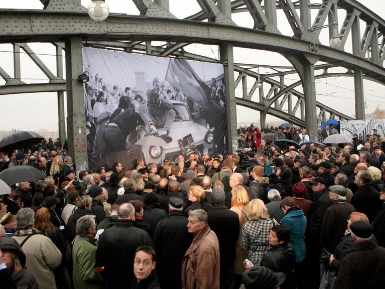 Das Bild zeigt wie an der Brücke an der Bornholmer Straße große Menschenmassen versuchen, einen Blick auf Bundeskanzlerin Angela Merkel, den ehemaligen Sowjetpräsidenten Michail Gorbatschow und den ehemaligen polnischen Solidaritätsführer Lech Walesa zum 20. Jahrestag des Mauerfalls am 9. November 2009 in Berlin zu werfen. Die drei Anführer sollten die Brücke und den darunter liegenden Bahnhof besuchen, weil dort 1989 die Wachen den ersten Grenzübergang öffneten und den Ostberlinern erlaubten, ungehindert nach Westberlin zu gehen.