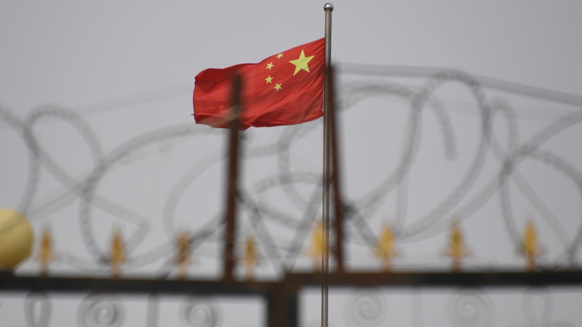 Die Flagge Chinas weht im Hintergrund. Im Vordergrund ist Stacheldraht zu sehen. Die Flagge Chinas weht im Hintergrund. Im Vordergrund ist Stacheldraht zu sehen.