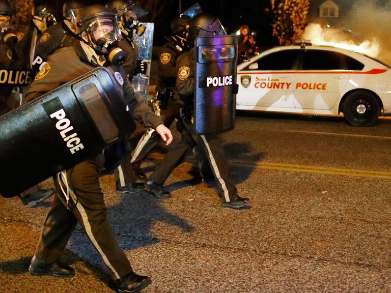 Polizisten mit Schutzschilden und Gasmasken vor einem brennenden Auto in Ferguson