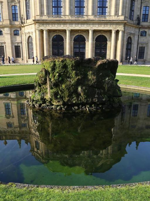 Spaziergänger gehen am 27.12.2015 im Hofgarten der Residenz in Würzburg (Bayern) hinter einem Brunnen entlang, in dem sich Teile der Residenz spiegeln.