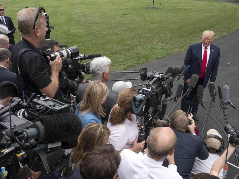 US-Präsident Trump steht vor einer Menschentraube von Journalisten auf einer Straße im Garten des Weißen Hauses. Die Reporter filmen und halten ihm Mikrofone entgegen.