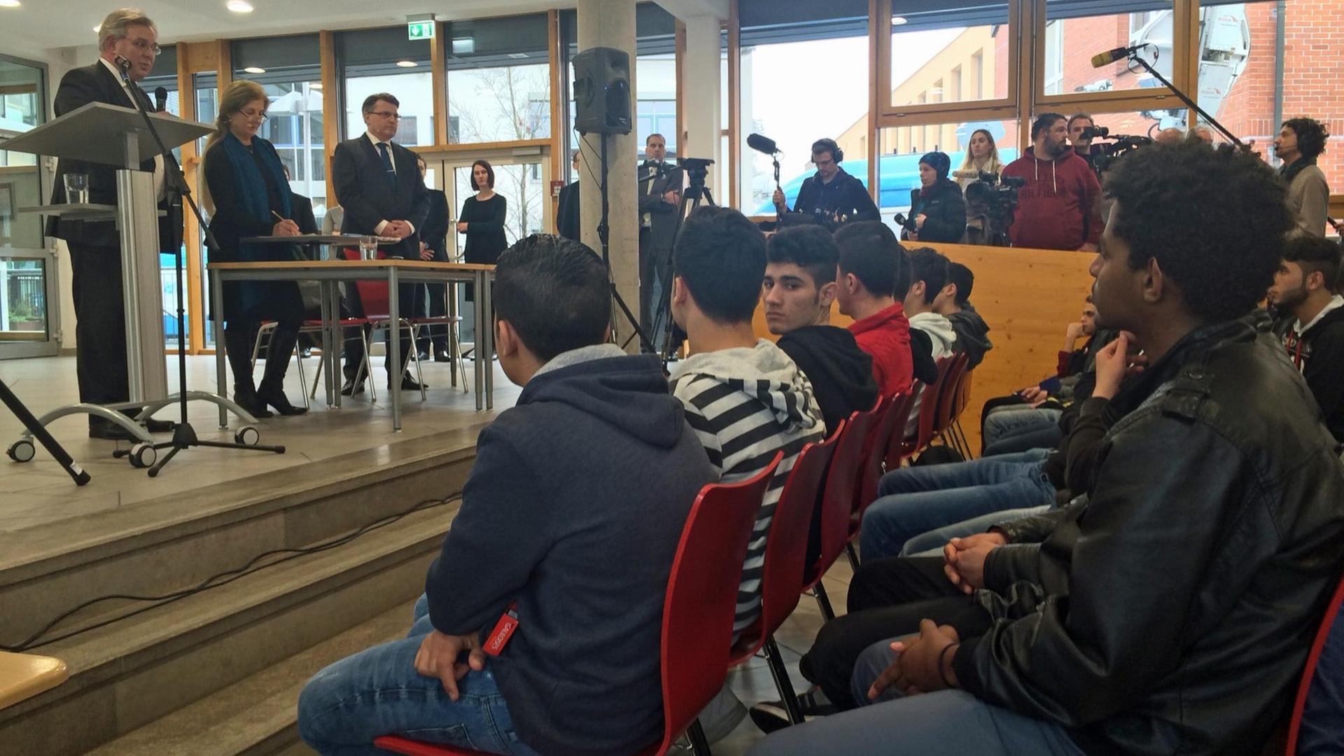 Flüchtlinge und Asylbewerber sitzen während eines Vortrag auf roten Stühlen.