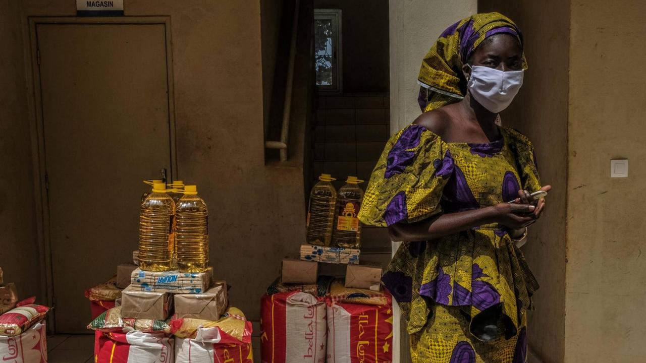 Eine Frau mit Maske vor Lebensmittelrationen, die an die Bevölkerungs im Senegal verteilt werden soll, die aufgrund von Coronamaßnahmen ihr Einkommen verloren haben.63