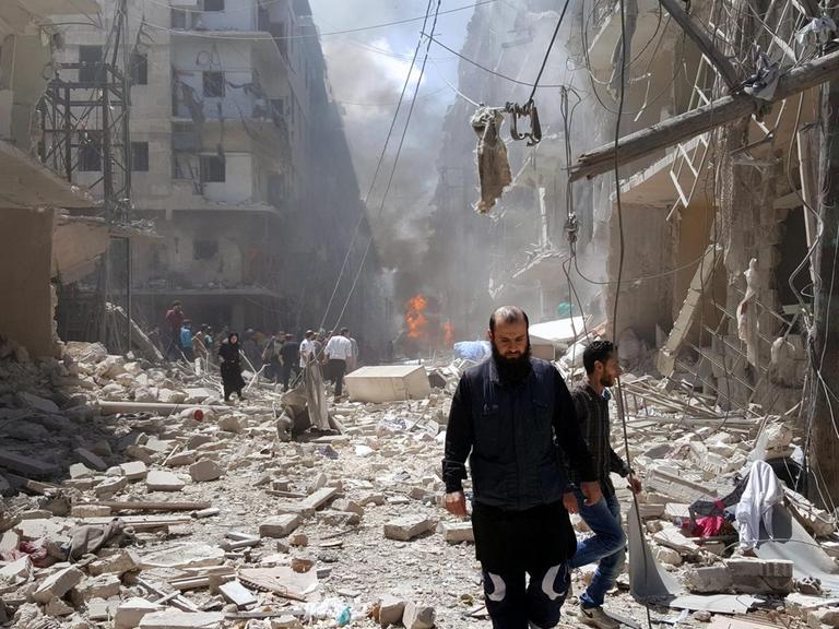 Der von Aufständischen kontrollierte Ostteil Aleppos wird durch Angriffe der syrischen Luftwaffe erschüttert. Sie sehen Syrer, die inmitten von Trümmern laufen.