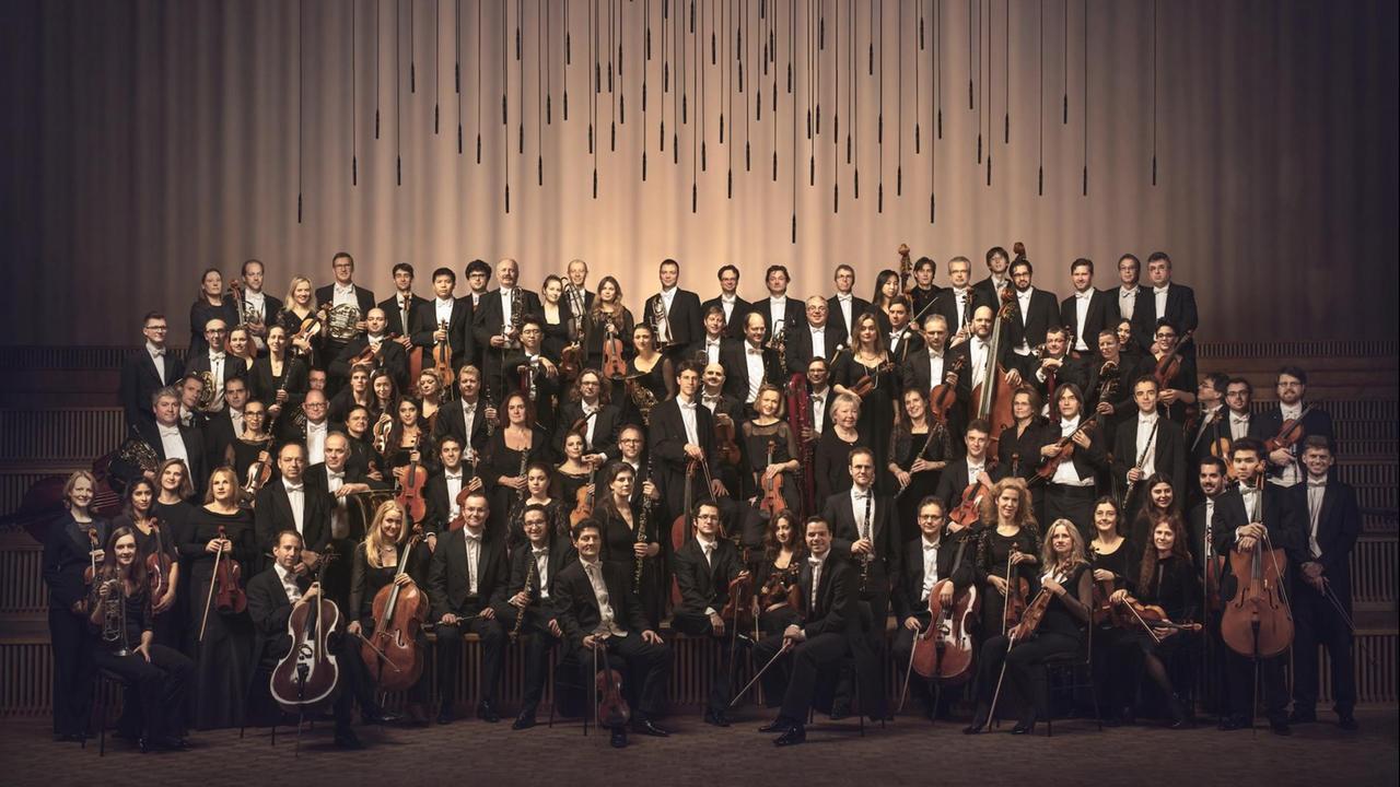 Die Musiker des Rundfunk-Sinfonieorchesters Berlin haben sich zu einem Gruppenfoto in einem Konzertsaal aufgestellt.