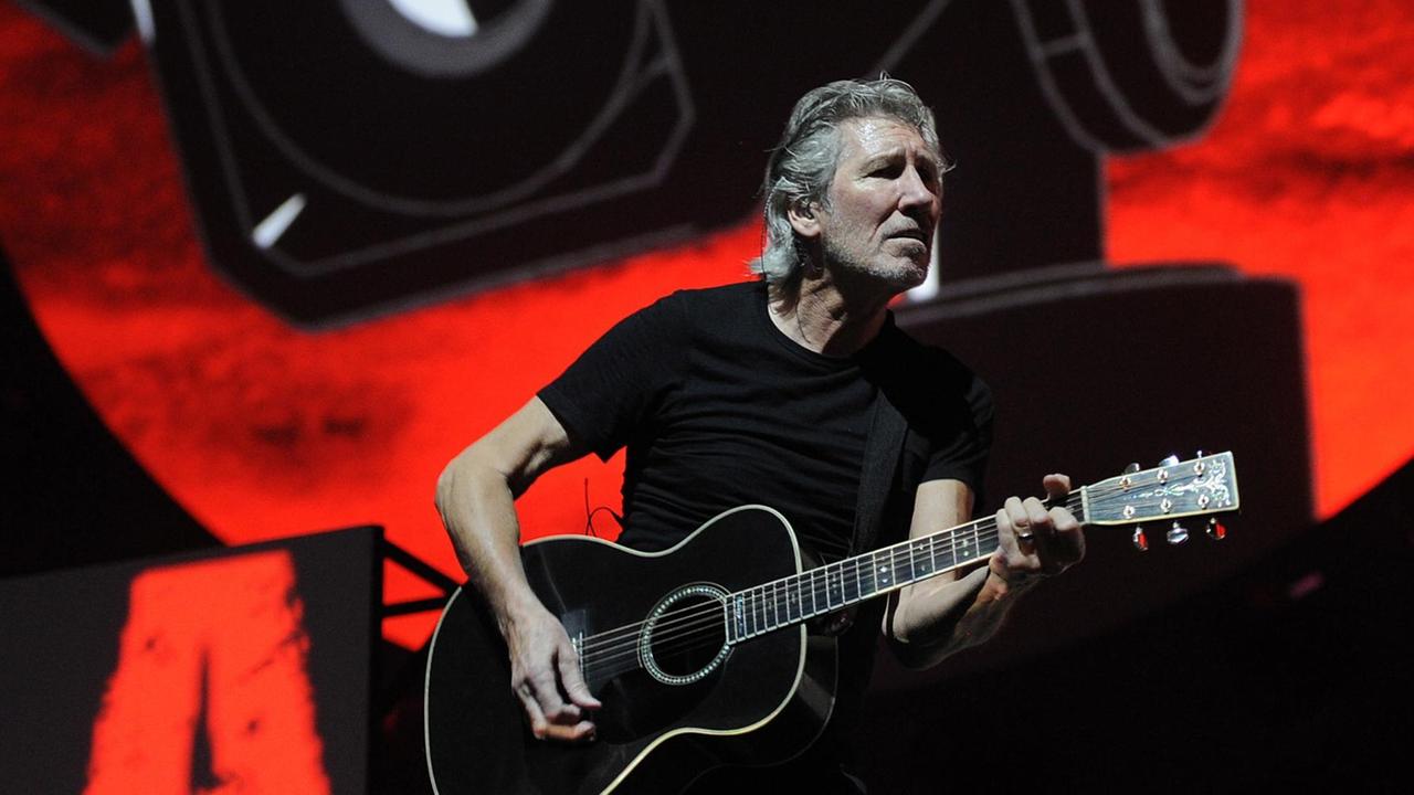 Roger Waters steht mit Gitarre auf einer Bühne