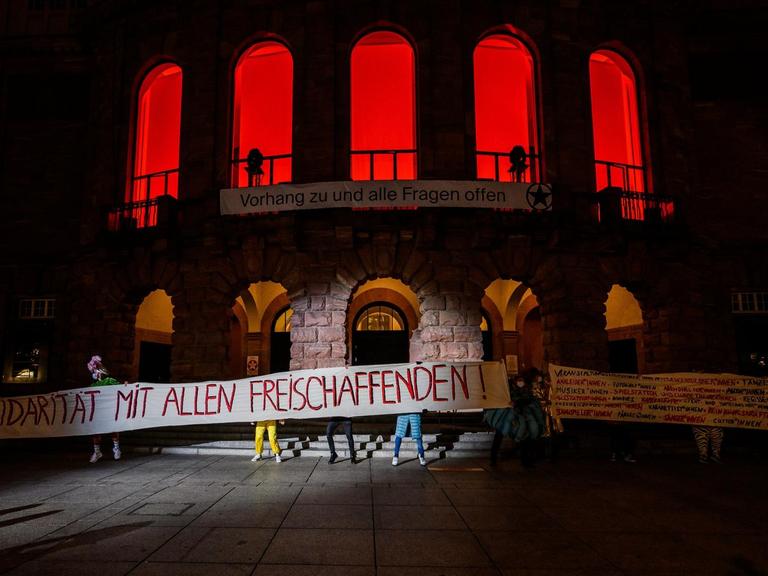 Die Künstler des Staatstheaters stehen mit einem Banner „Solidarität mit allen Freischaffenden!“ vor dem Haus.