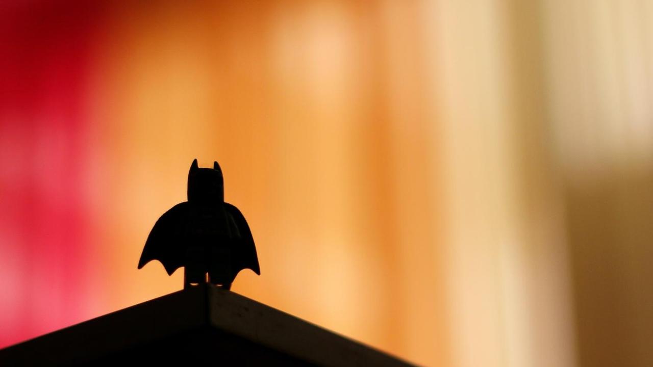 Die Silhouette einer Batman-Legofigur hebt sich dunkel vor einem unscharfen Bildhintergrund ab.