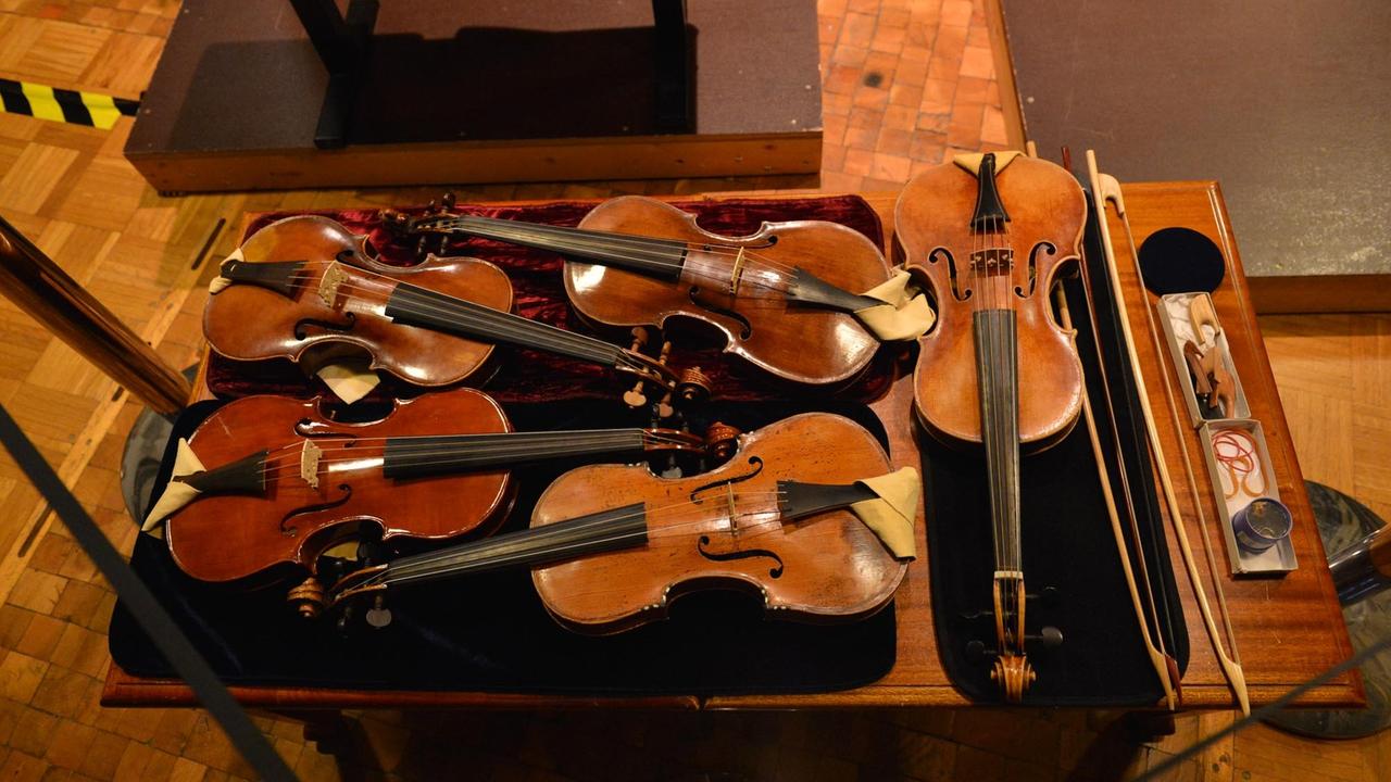 Fünf barocke Geigen und zwei historische Bögen liegen nebeneinander auf einem Tisch
