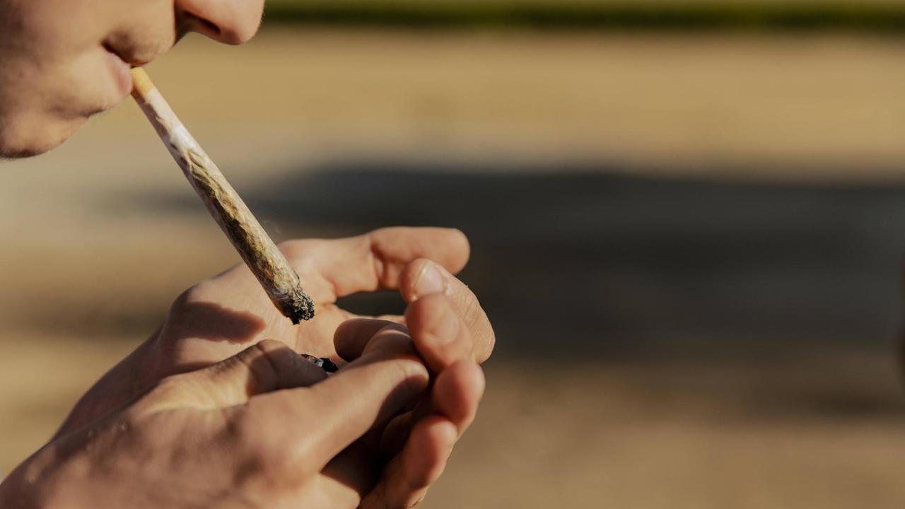 Ein Jugendlicher, von dem man nur Nase und Mundpartie sieht, zündet sich einen Joint an.