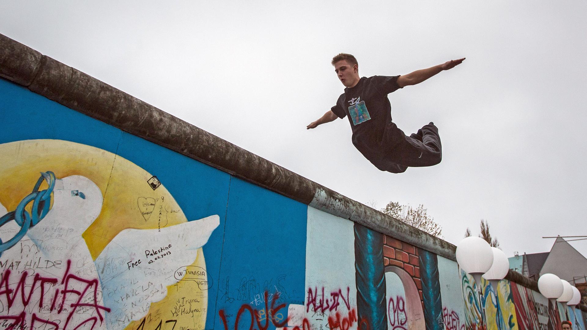 Ein Jugendlicher im Sprung über der Berliner Mauer. Jugendliche treten am 09.11.2014 in Berlin an der East Side Gallery in einer Vorstellung des Cabuwazi Zirkus und der Hochseilgruppe Geschwister Weisheit mit dem Titel "Zirkus berwindet Grenzen" auf.