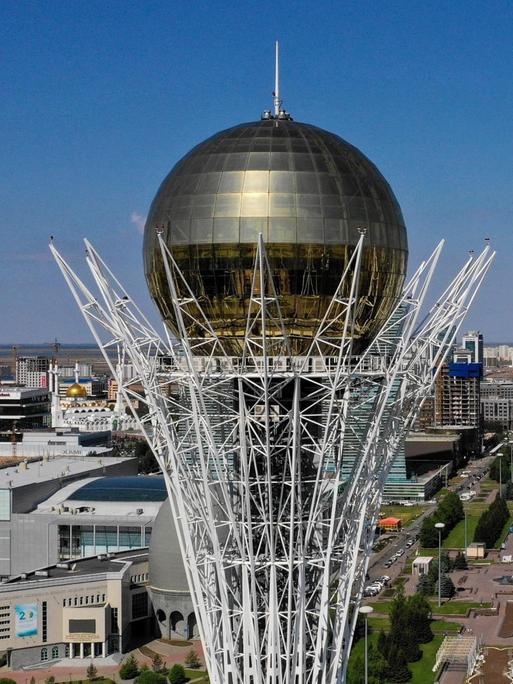 Luftansicht von Nur-Sultan in Kasachstan, futuristische Hochhäuser und im Vordergrund ein Monument mit großer goldener Kugel auf der Spitze