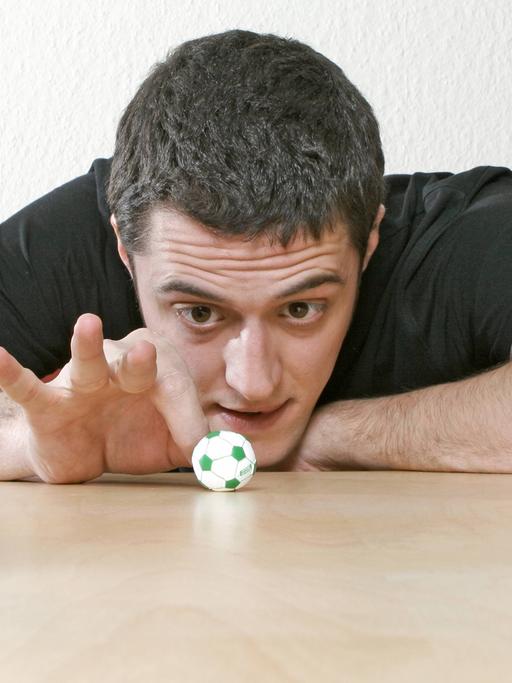 Ein junger Mann spielt mit einem Minifussball zwischen zwei Bierflaschen