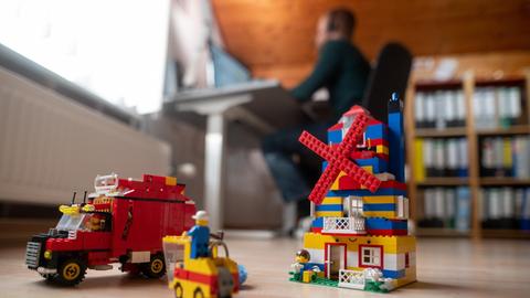Ein Mann arbeitet im Homeoffice, während im Vordergrund Spielzeug seiner Kinder steht.